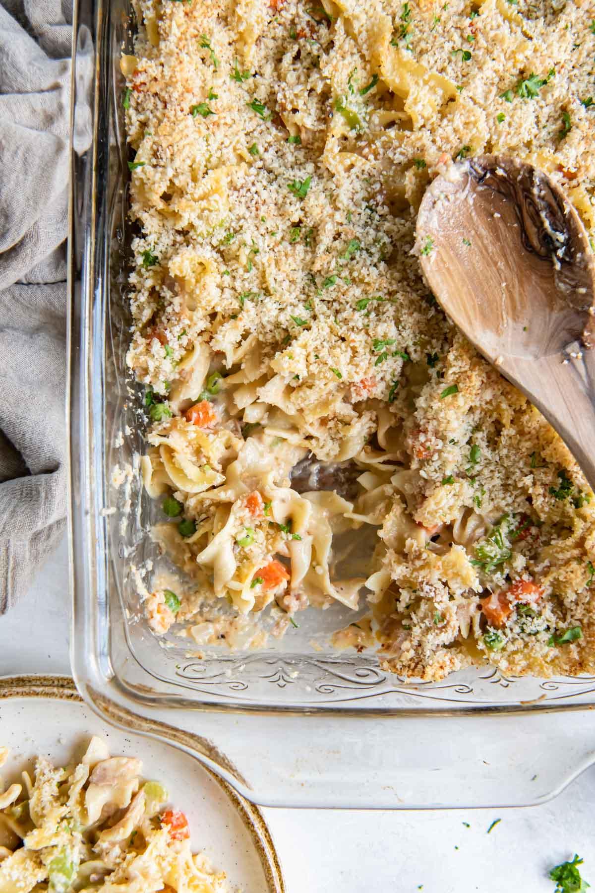A golden brown and bubbly tuna noodle casserole in a baking dish, garnished with fresh parsley