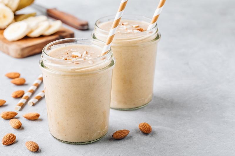 Close-up shot of a creamy almond and vanilla smoothie in a glass with almonds and vanilla bean scattered around