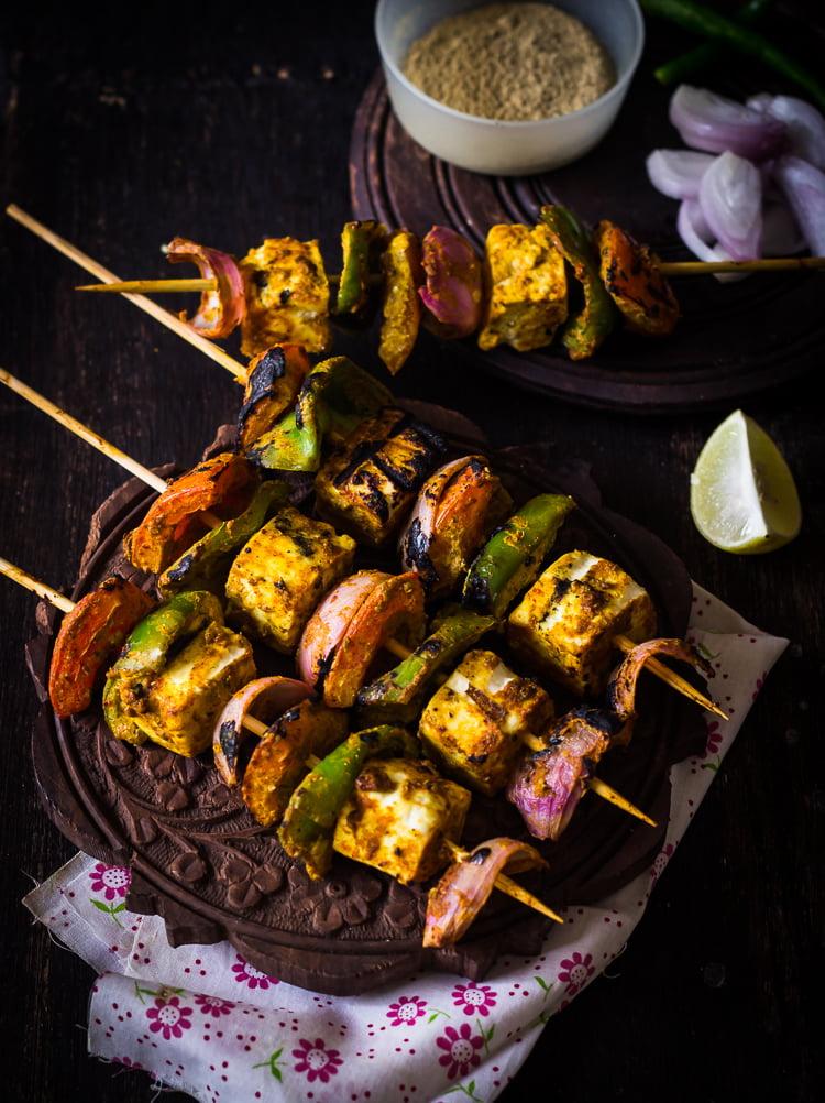 Close-up shot of tandoori paneer tikka skewers served with vibrant green mint chutney