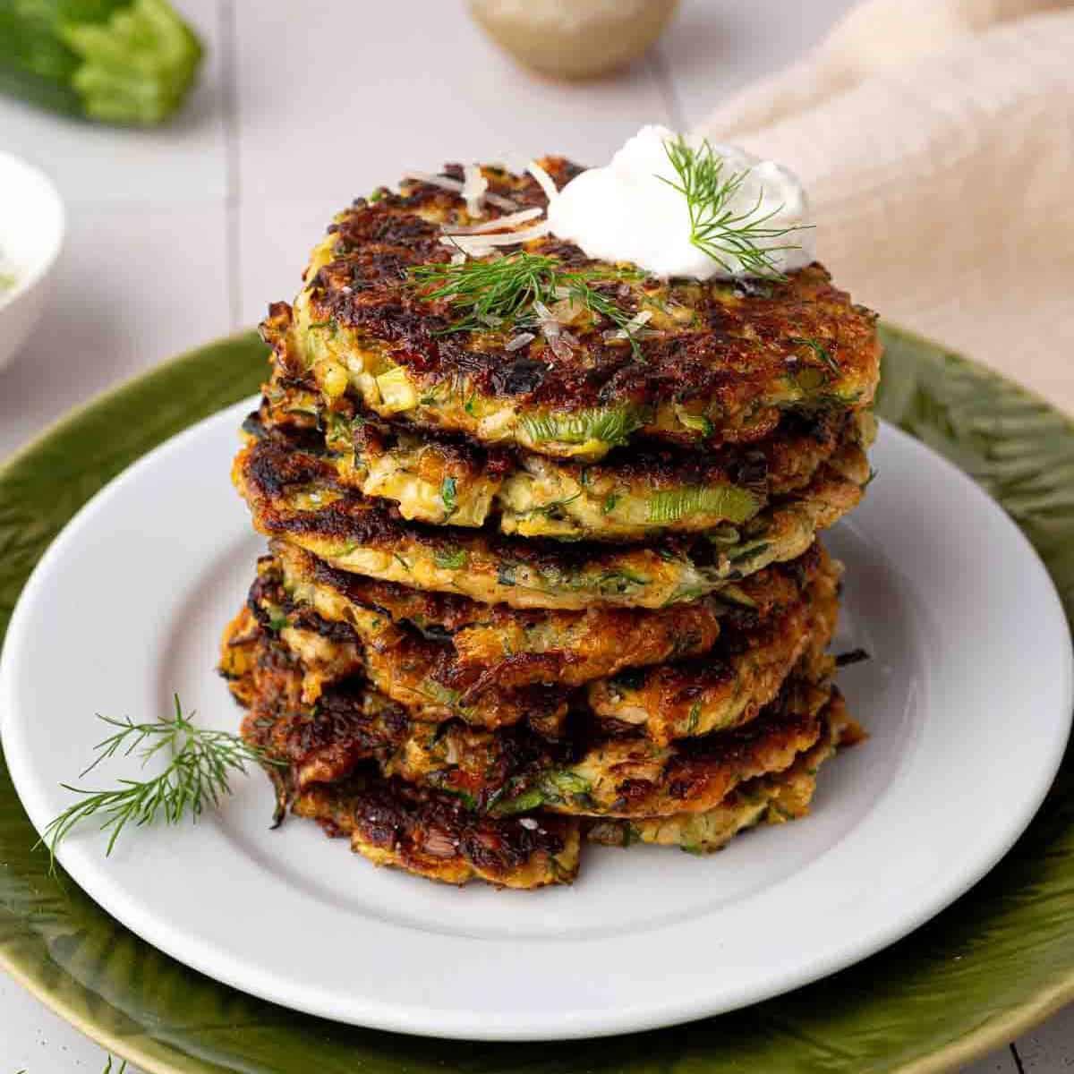 golden brown baked zucchini fritters with fresh herb yogurt dip, garnished with dill