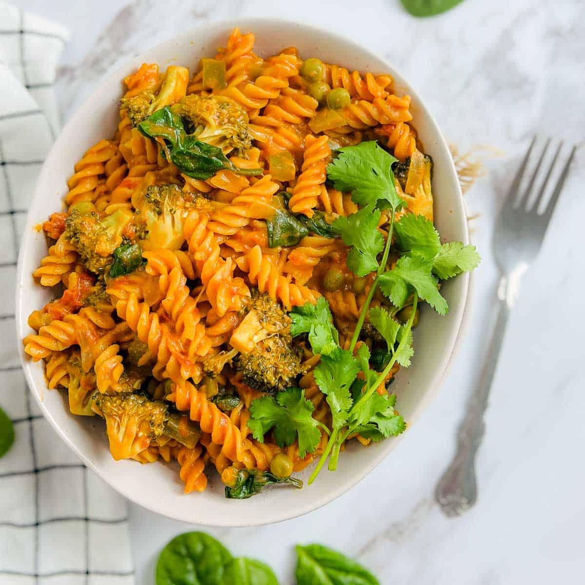 A bowl of gluten-free pasta with lentil and vegetable curry, garnished with fresh herbs