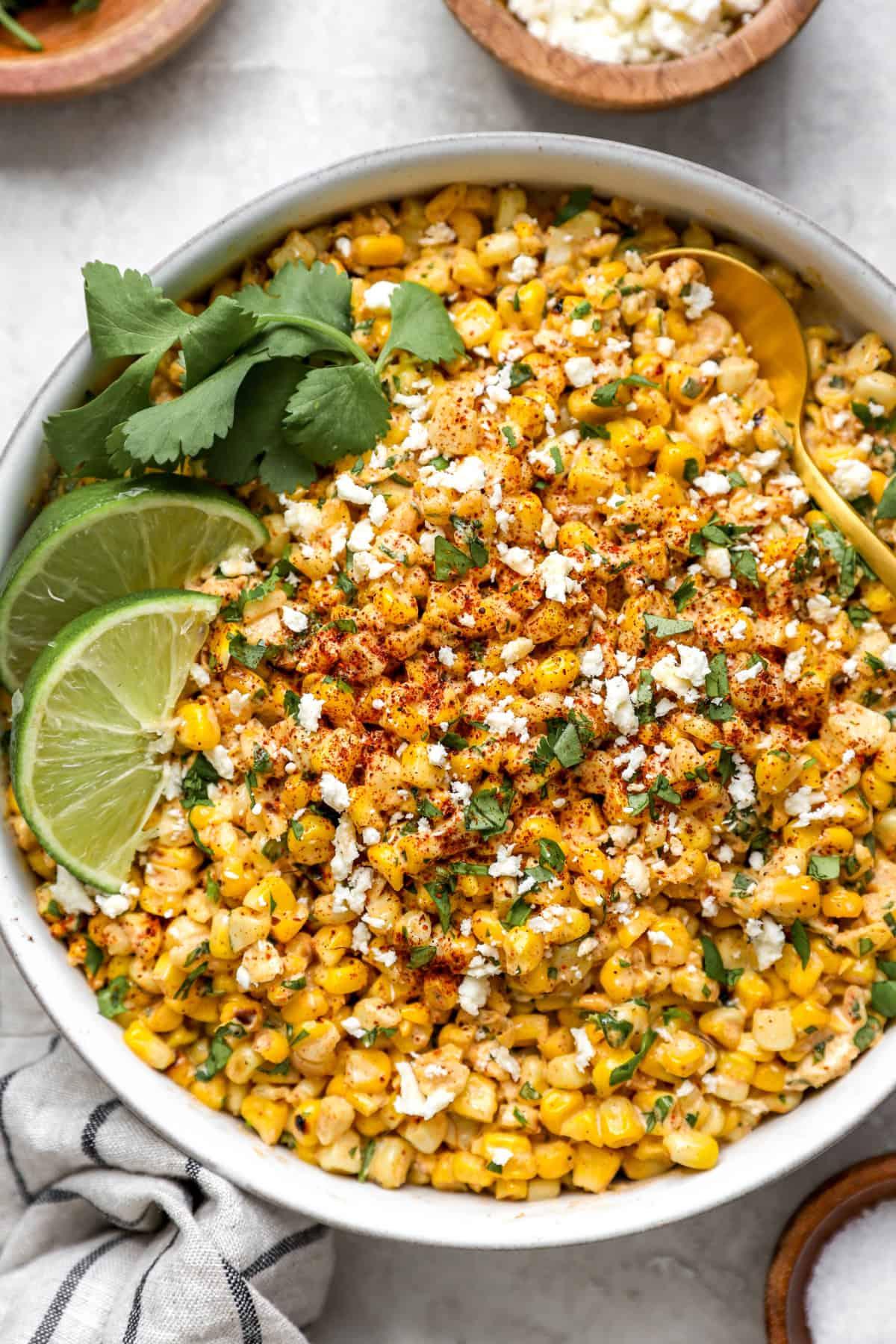 Cilantro corn salad served in a bowl, garnished with lime wedges