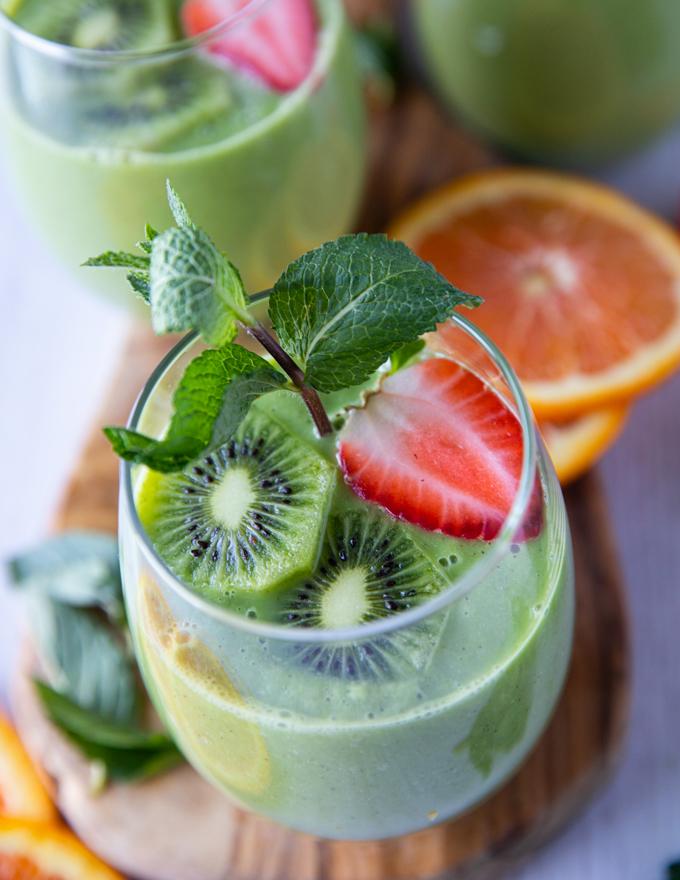 overhead shot of a blended green smoothie with fresh berries and spinach visible, garnished with mint