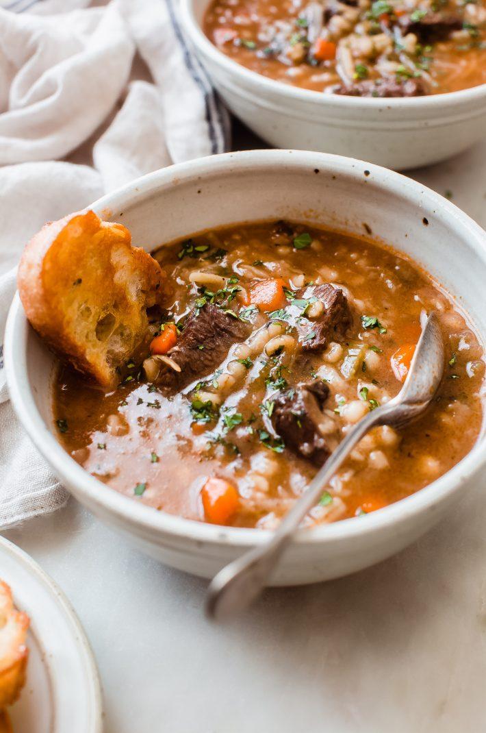A rustic wooden table set with a bowl of Instant Pot Beef and Barley Stew, crusty bread, and a glass of red wine.