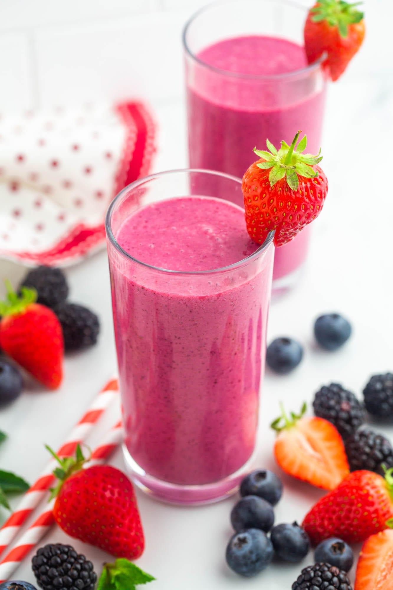 vibrant pink and red berry smoothie in a glass with fresh berries on the side