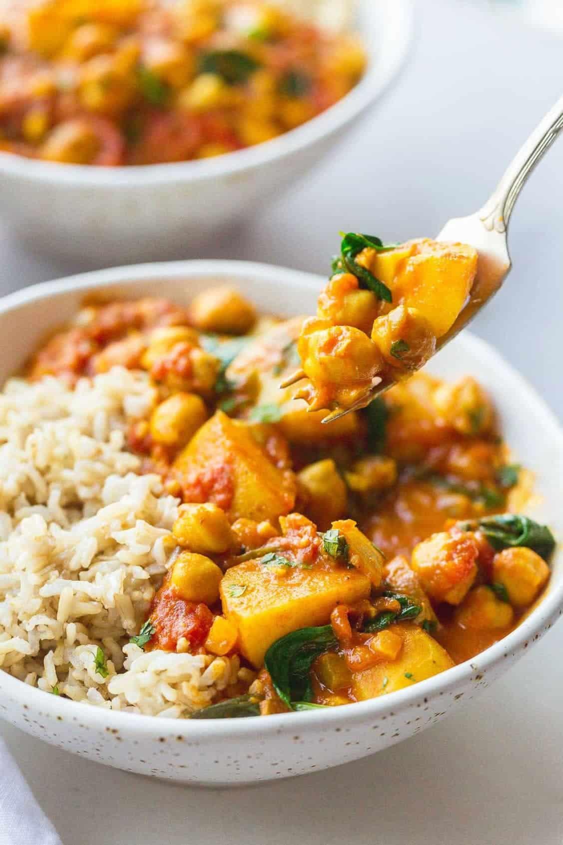 A person serving a bowl of chickpea and potato curry to a family