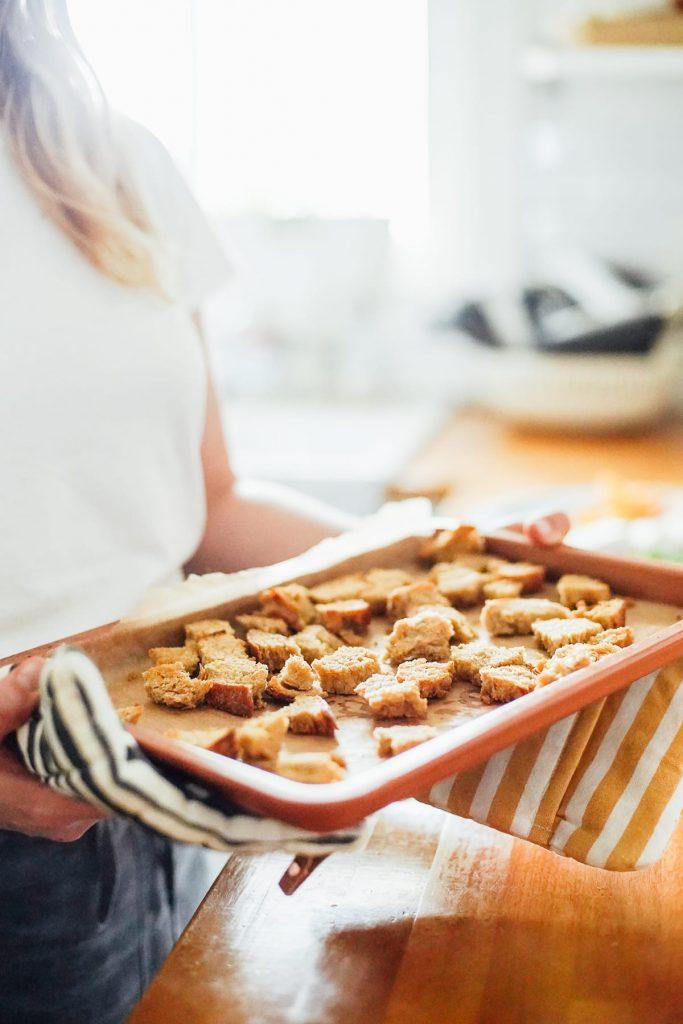 A person tossing homemade croutons on a baking sheet