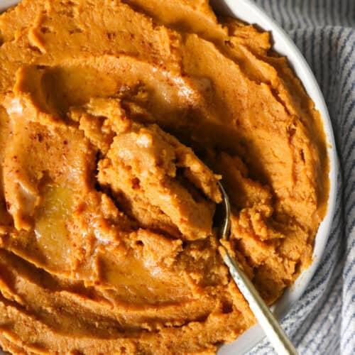 Close-up of creamy mashed sweet potato mixture in a bowl with spices.