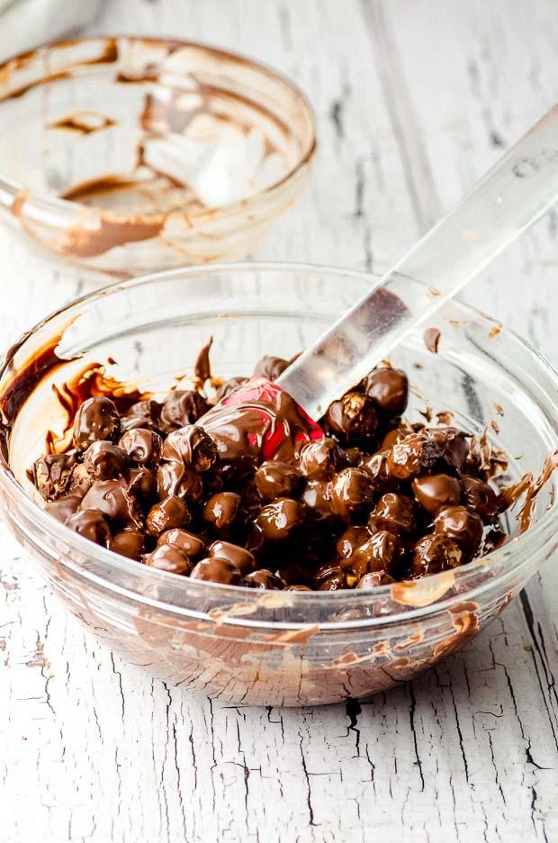 Hands carefully coating roasted hazelnuts with melted chocolate