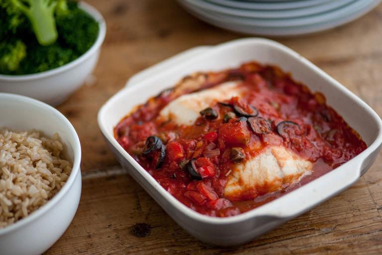 A rustic table setting featuring a plate of sautéed cod with tomato sauce