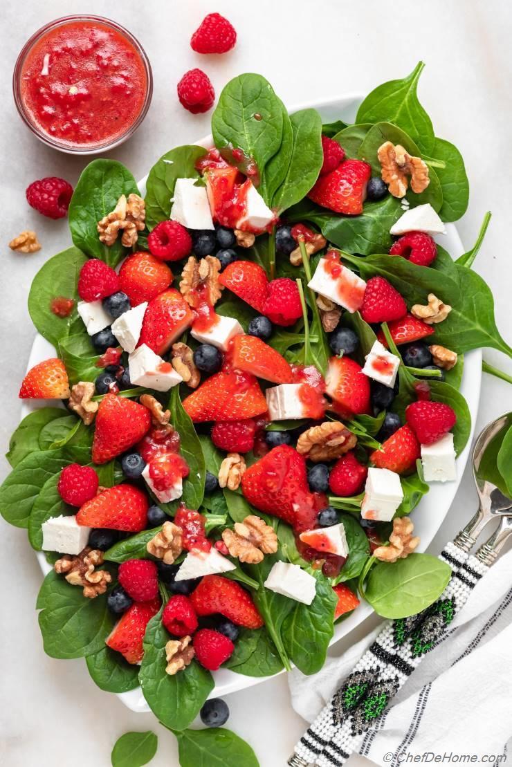 A vibrant strawberry spinach salad with a raspberry vinaigrette dressing, garnished with fresh raspberries