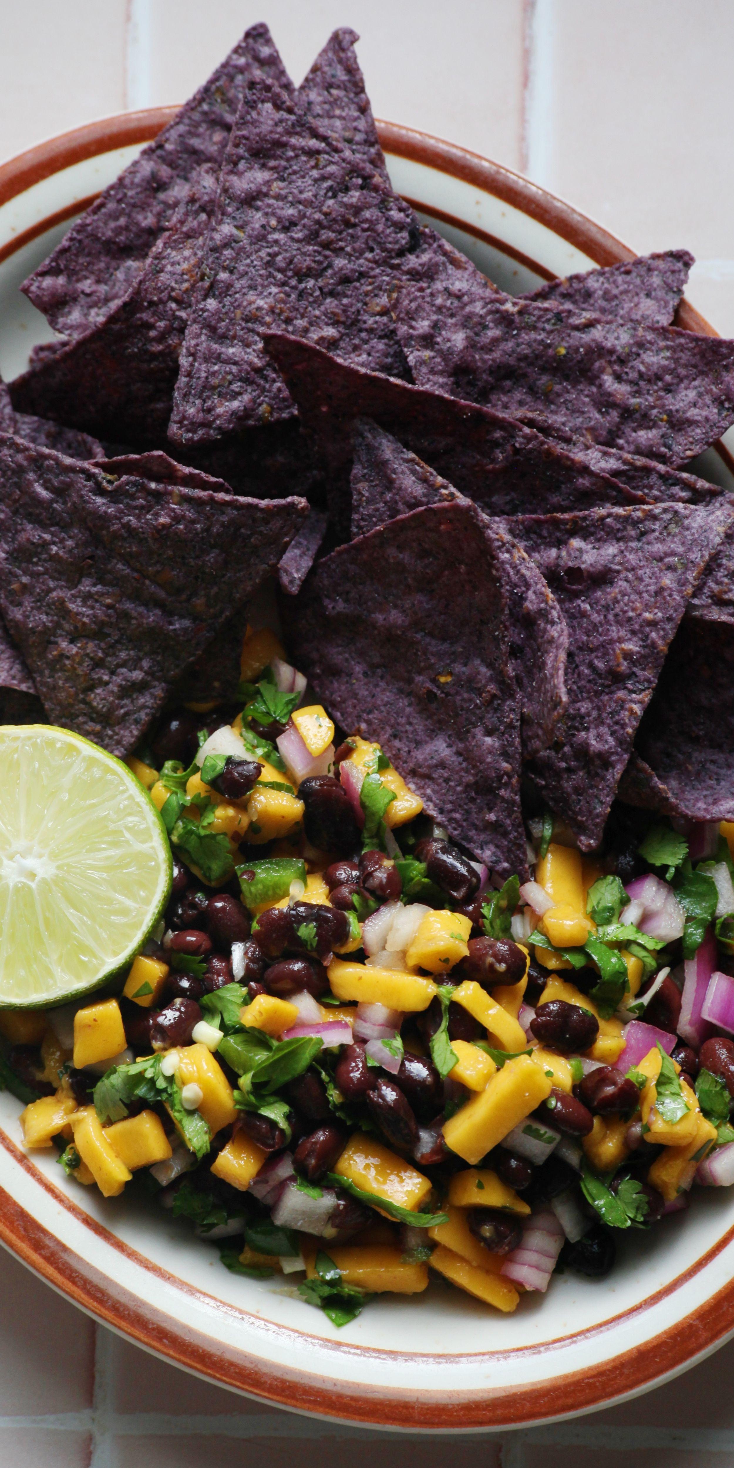 close up shot of a person scooping black bean and mango salsa with a plantain chip