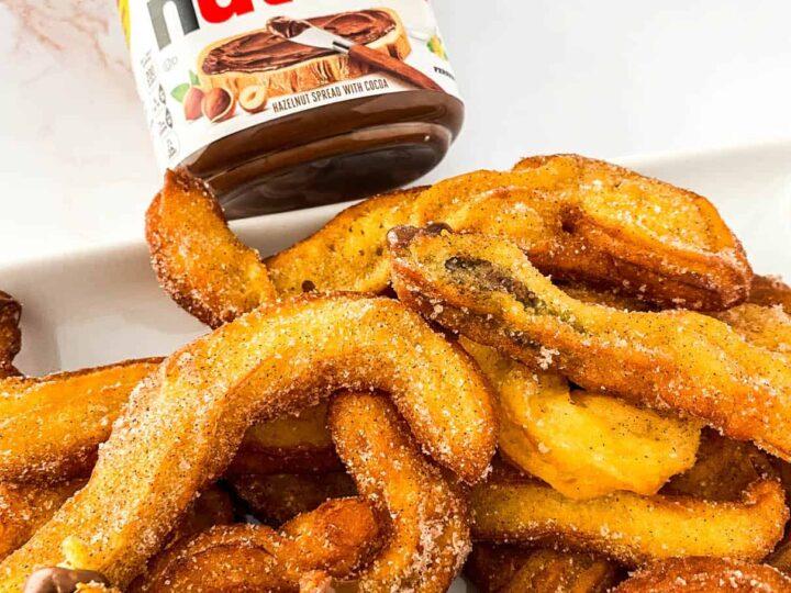 A close up of a golden-brown churro being piped with Nutella filling