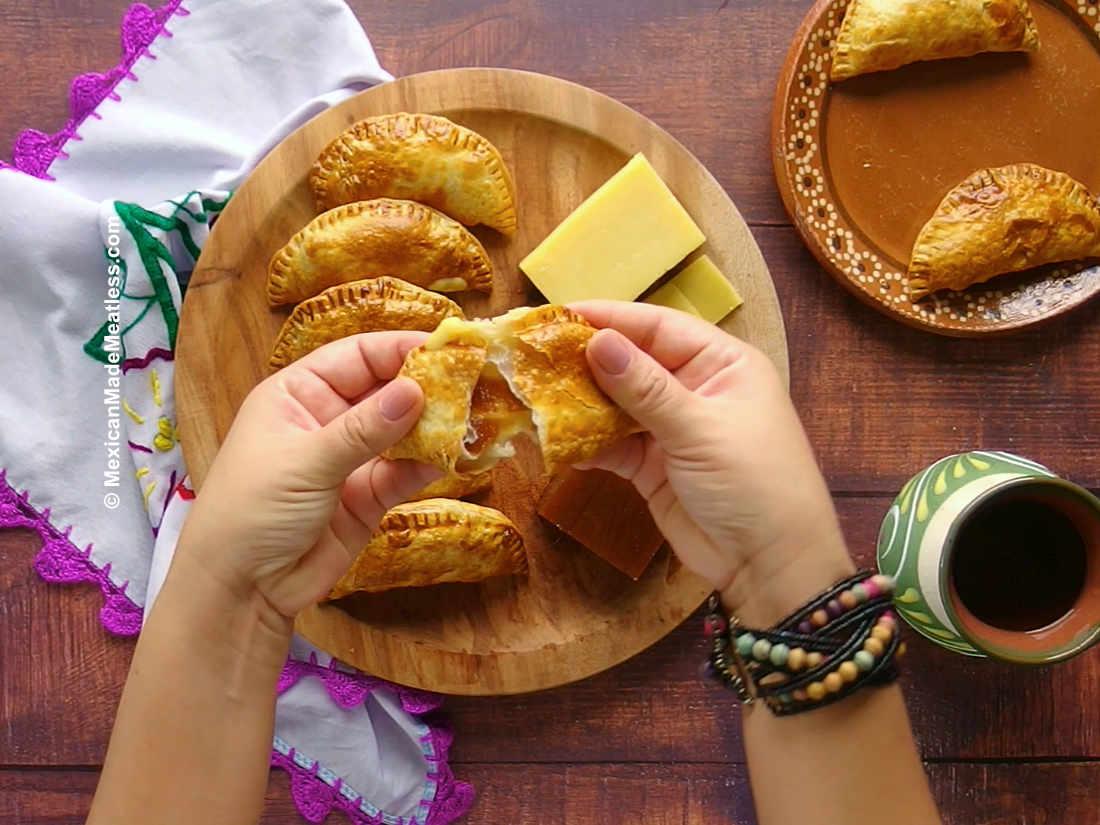 Golden brown guava and cheese empanadas on a rustic wooden board, garnished with fresh mint leaves and a sprinkle of powdered sugar