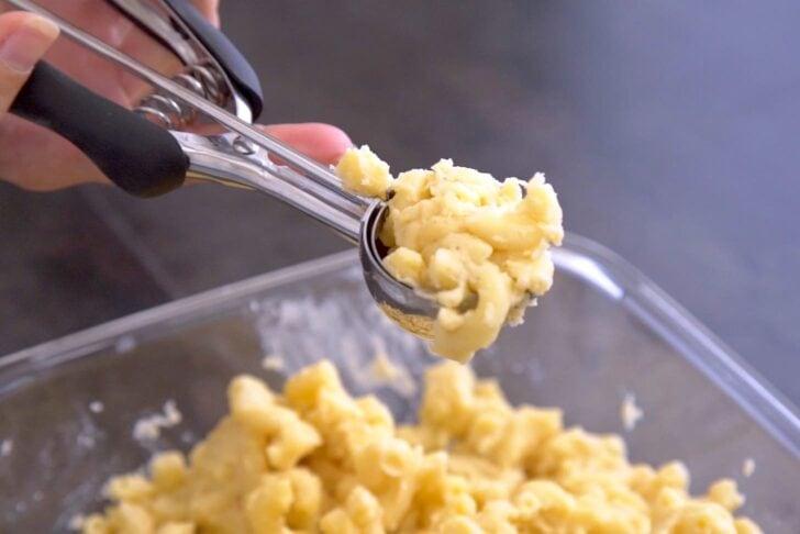 a hand reaching into a baking dish of extra cheesy macaroni and cheese, pulling out a cheesy bite
