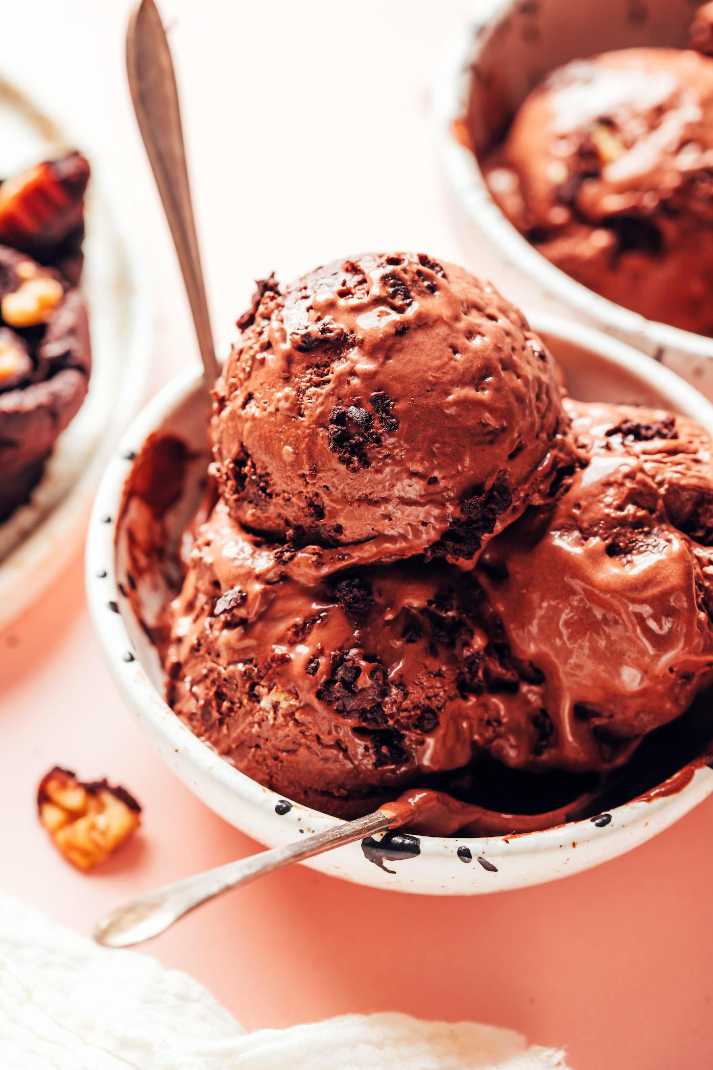a bowl of vegan chocolate brownie ice cream with a spoon, topped with brownie pieces