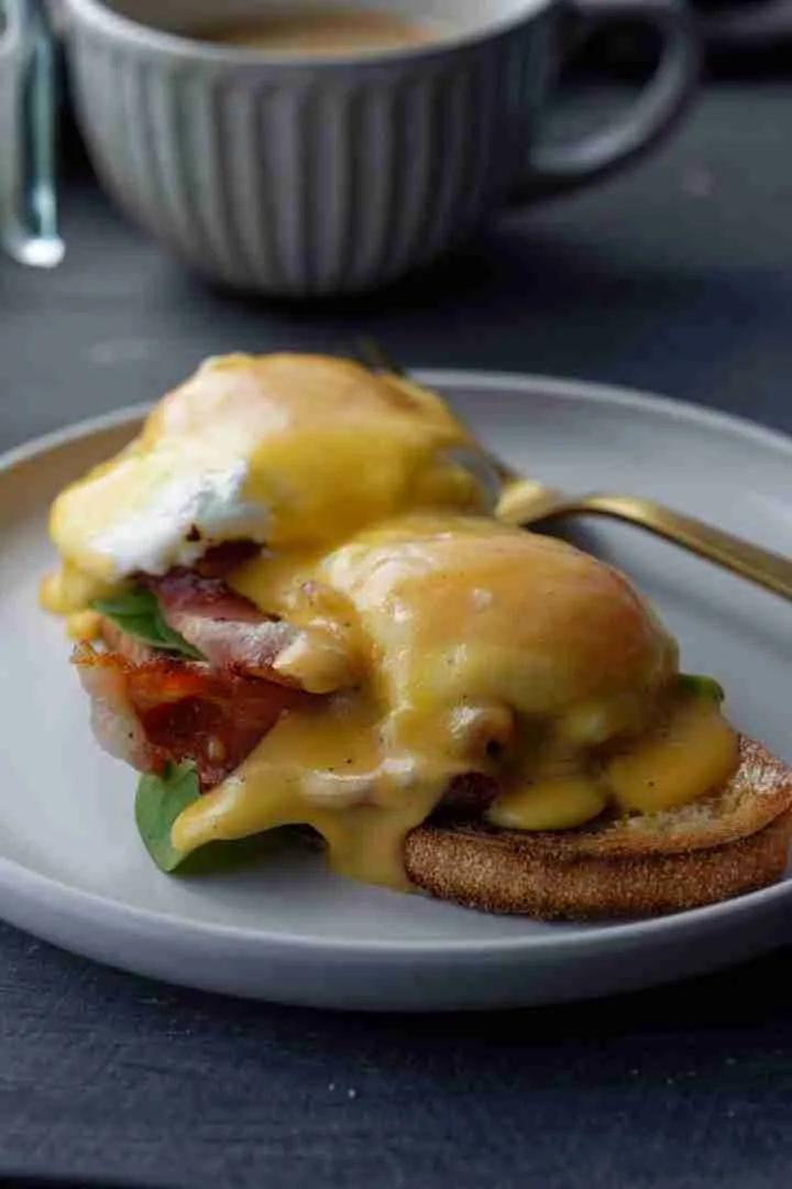 A close-up of the parsley hollandaise sauce being drizzled over the Eggs Benedict.