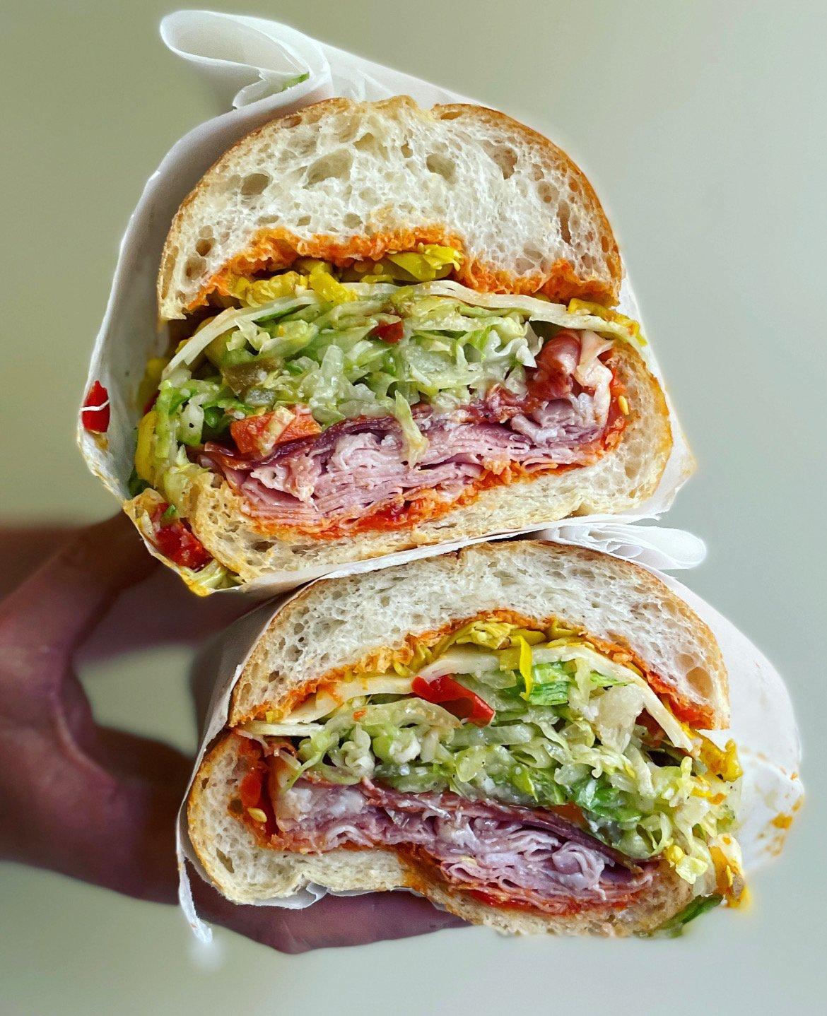 A close-up shot of a delicious Italian hoagie wrap, cut in half, showcasing the layers of meat, cheese, vegetables, and giardiniera.