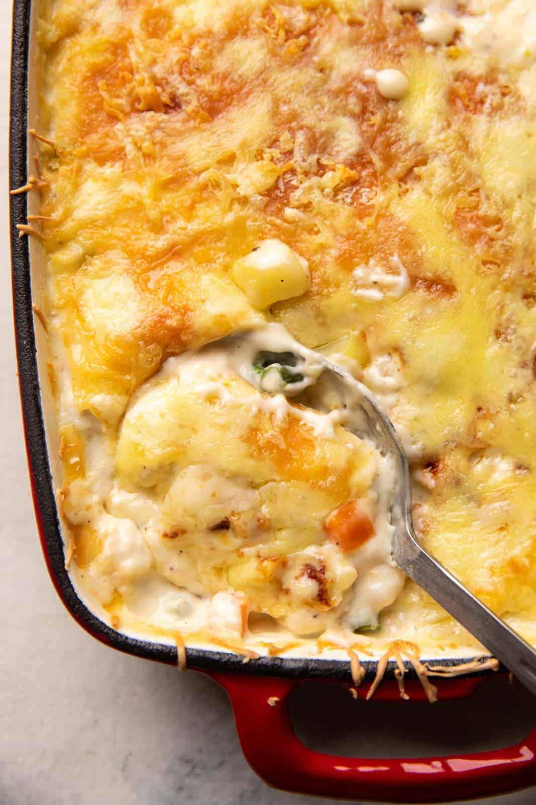 A close-up shot of a creamy, golden béchamel sauce being poured over layers of vegetables in an ovenproof dish.