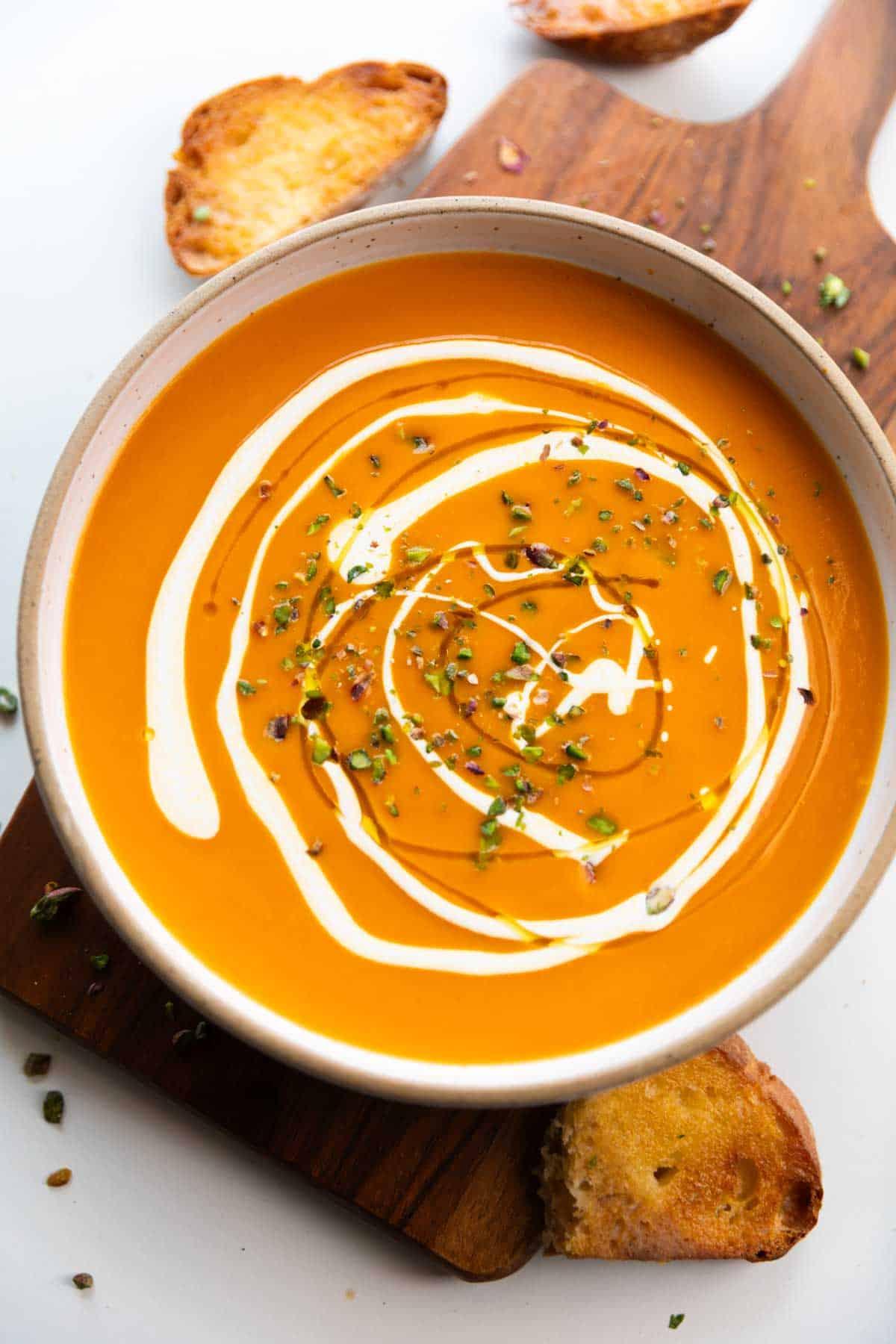 Close-up shot of a rustic bowl filled with creamy pumpkin soup, roasted red peppers peeking through, garnished with pumpkin seeds and a swirl of cream.