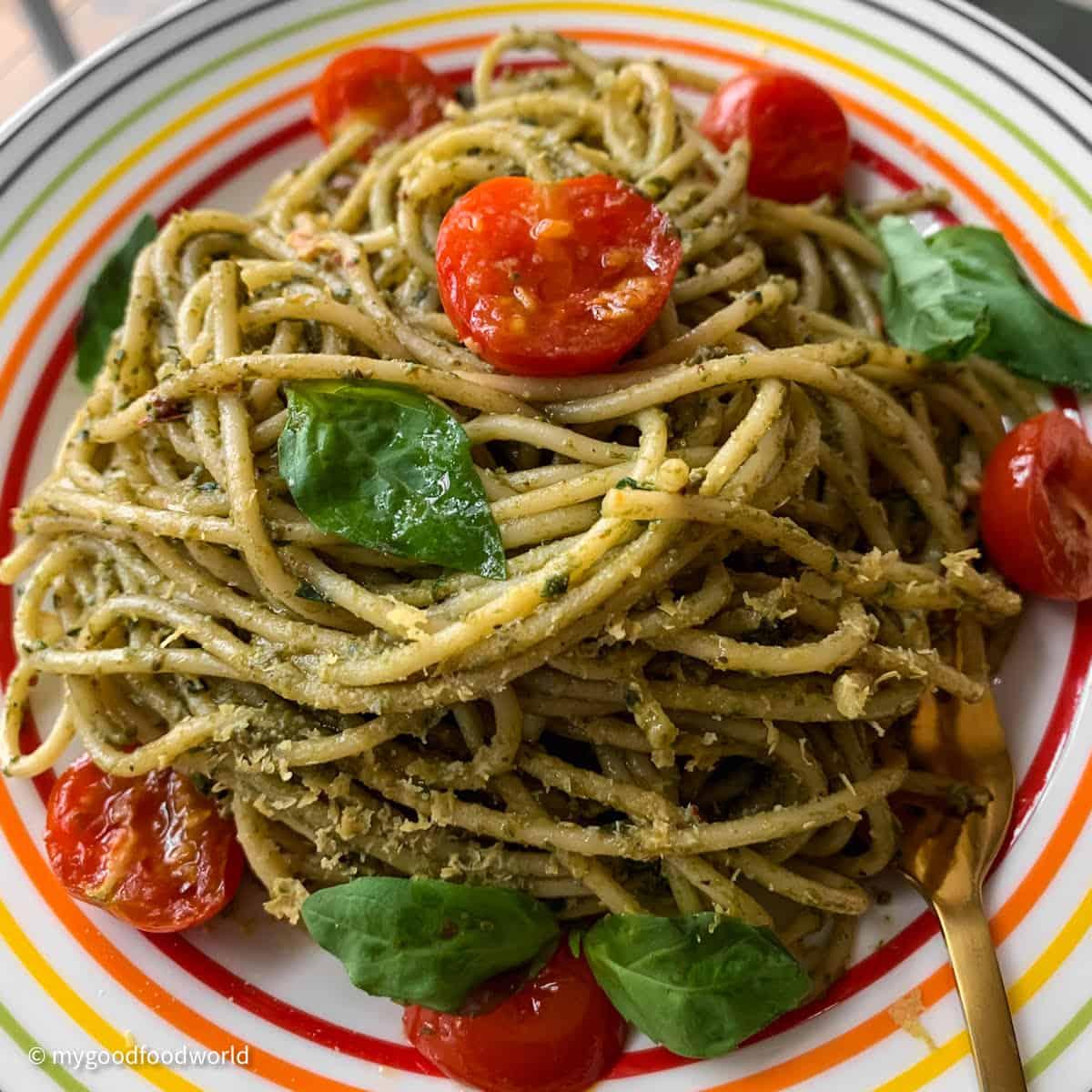 A vibrant close-up of a plate of gluten-free pasta with bright green pesto, garnished with fresh basil leaves and cherry tomatoes.