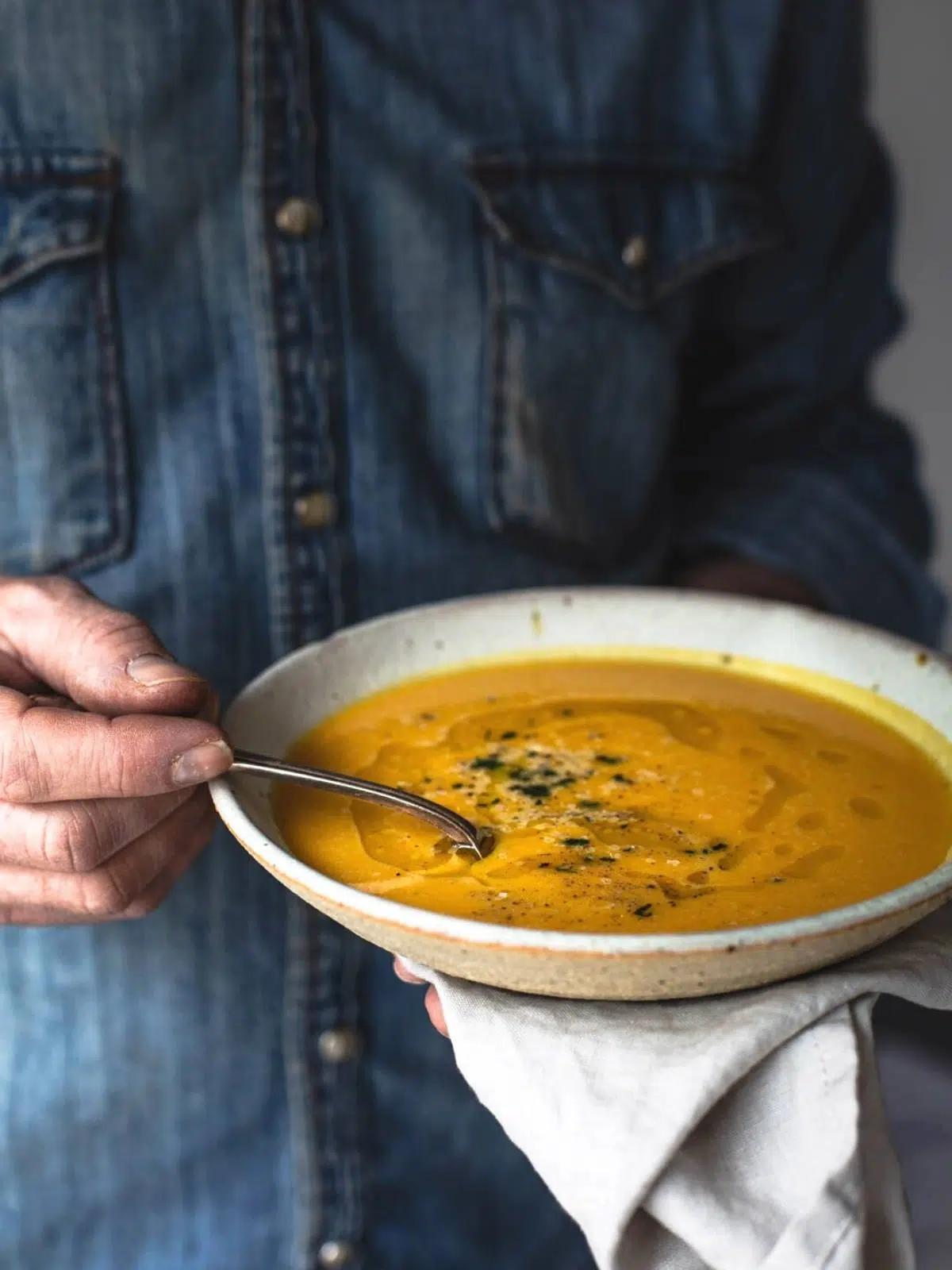 A person happily stirring a pot of pumpkin soup