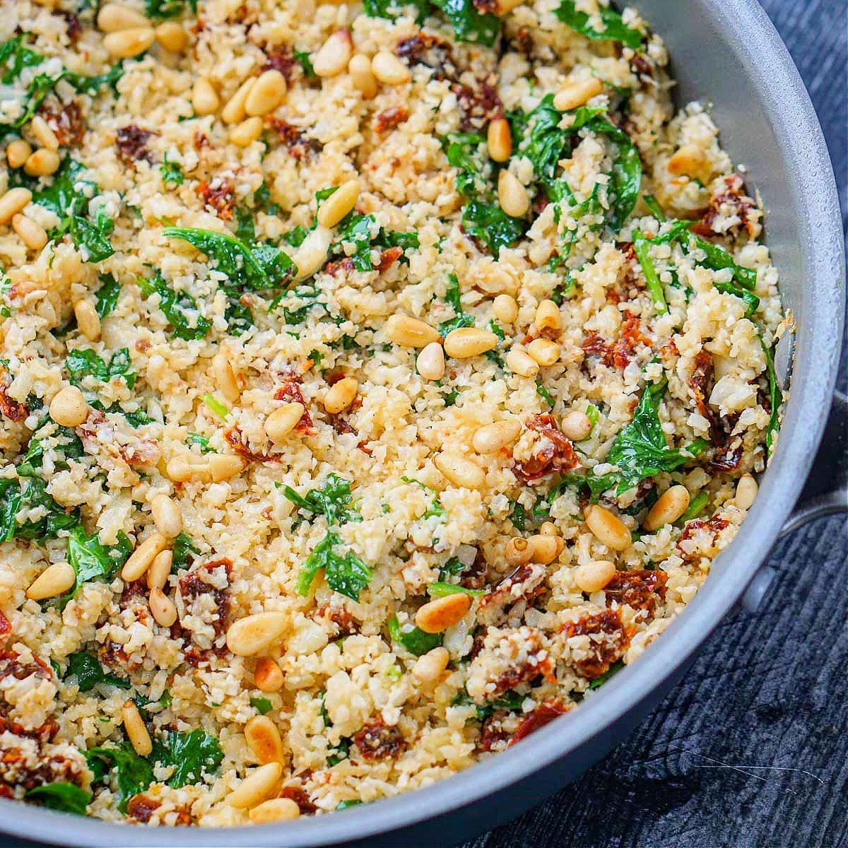 A vibrant close-up shot of cauliflower rice tossed with pesto and sun-dried tomatoes, garnished with fresh basil.