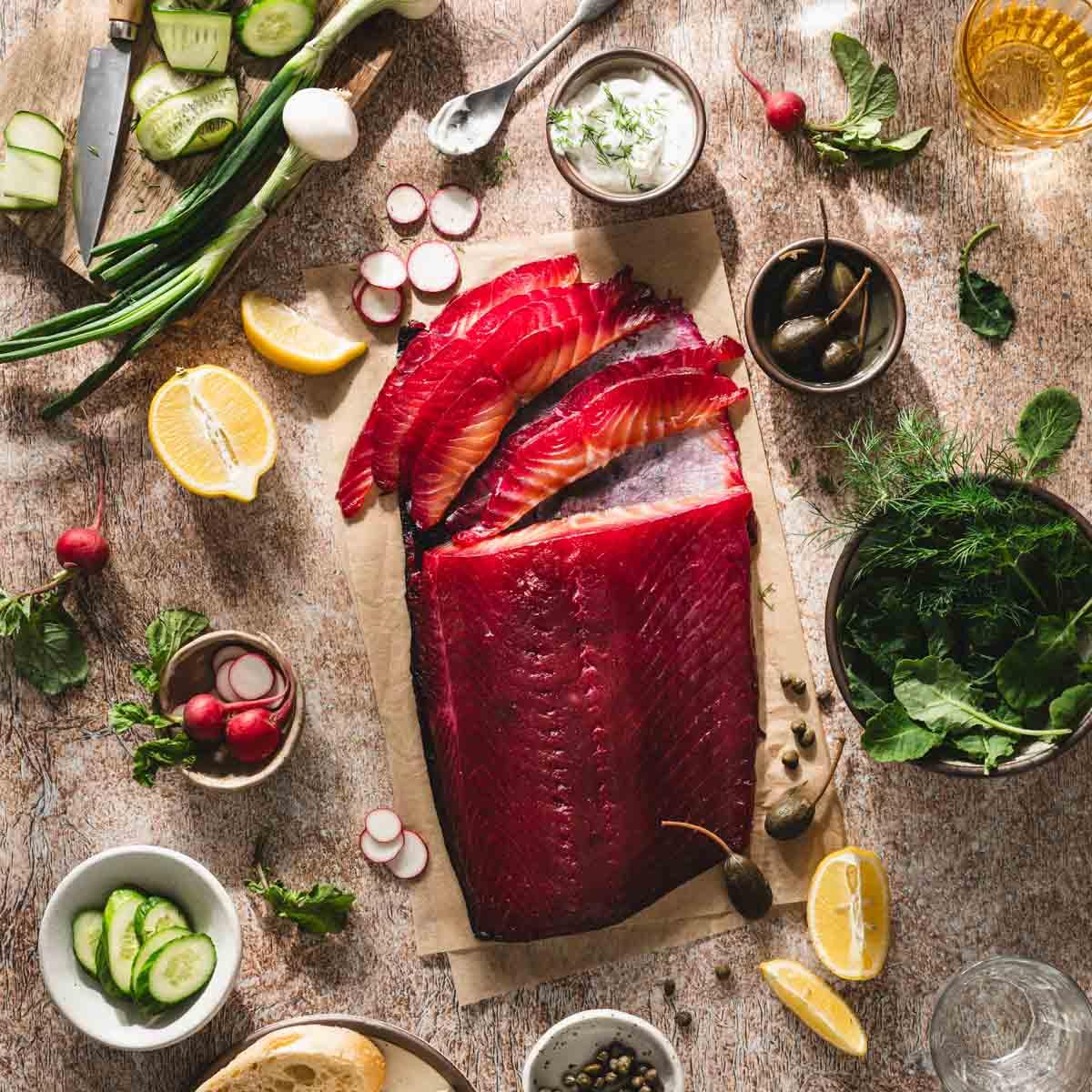 Overhead shot of prepared gravlax ingredients: salmon fillet, beetroot, horseradish, salt, sugar, peppercorns.