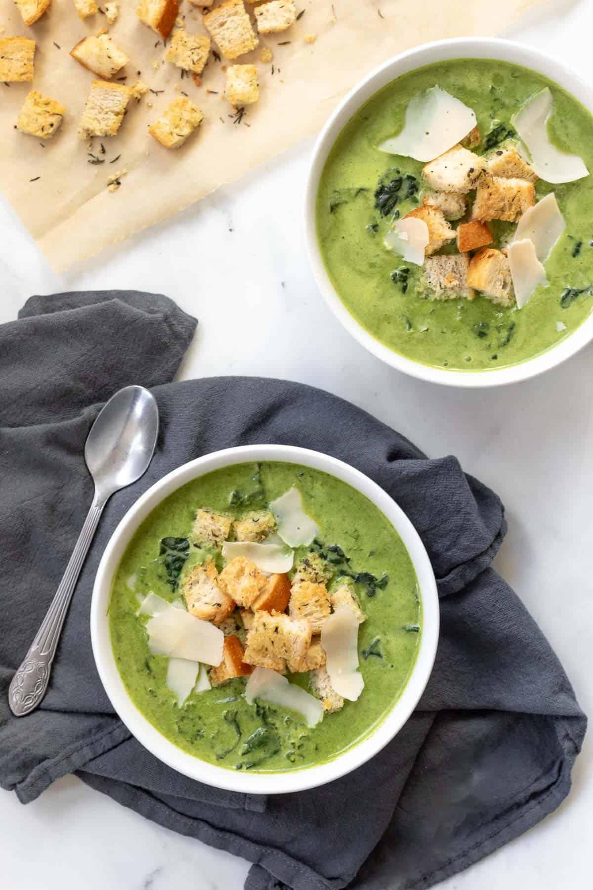 Close-up shot of a bowl of creamy kale and spinach soup, garnished with fresh herbs and a swirl of coconut milk