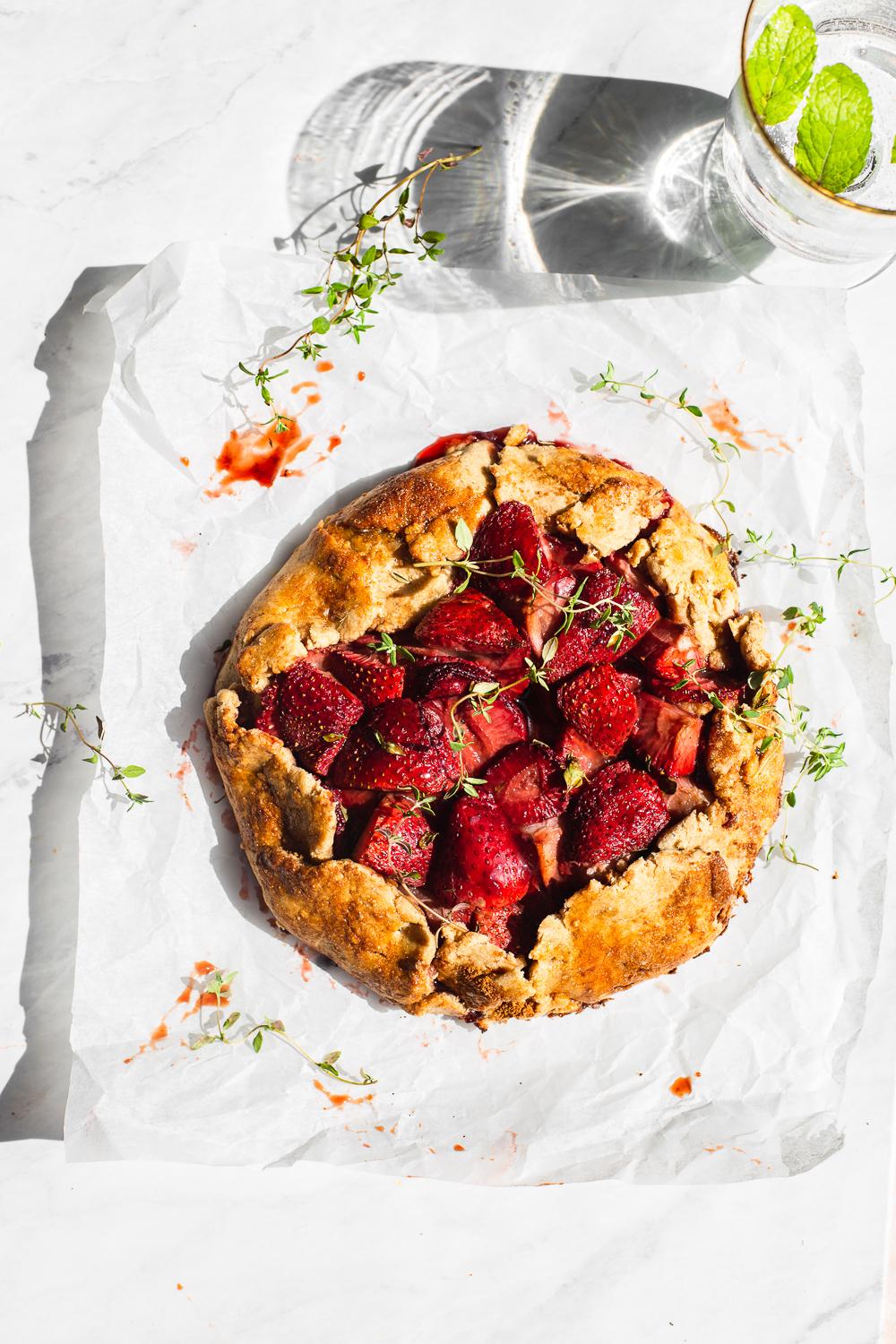 A rustic galette being sliced and served on a wooden table, garnished with fresh thyme