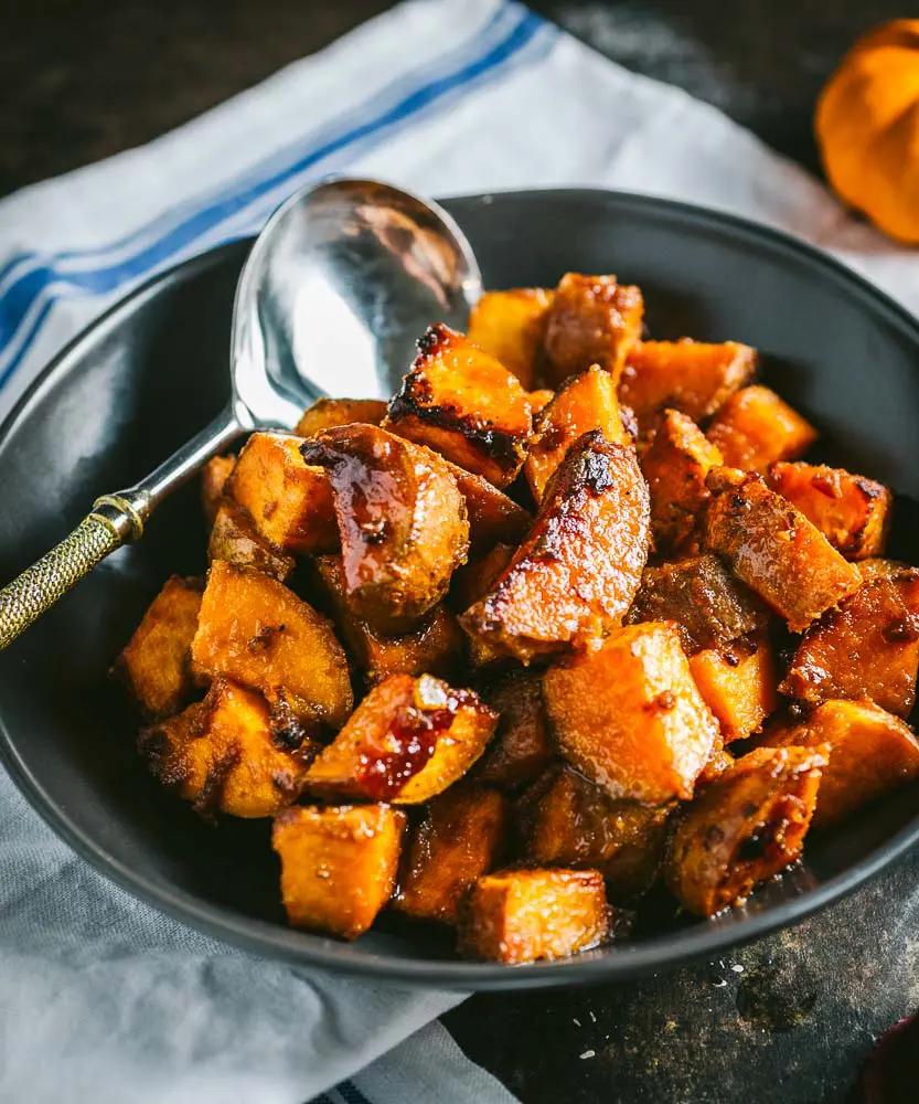 A rustic wooden table with a bowl of roasted sweet potatoes and maple syrup