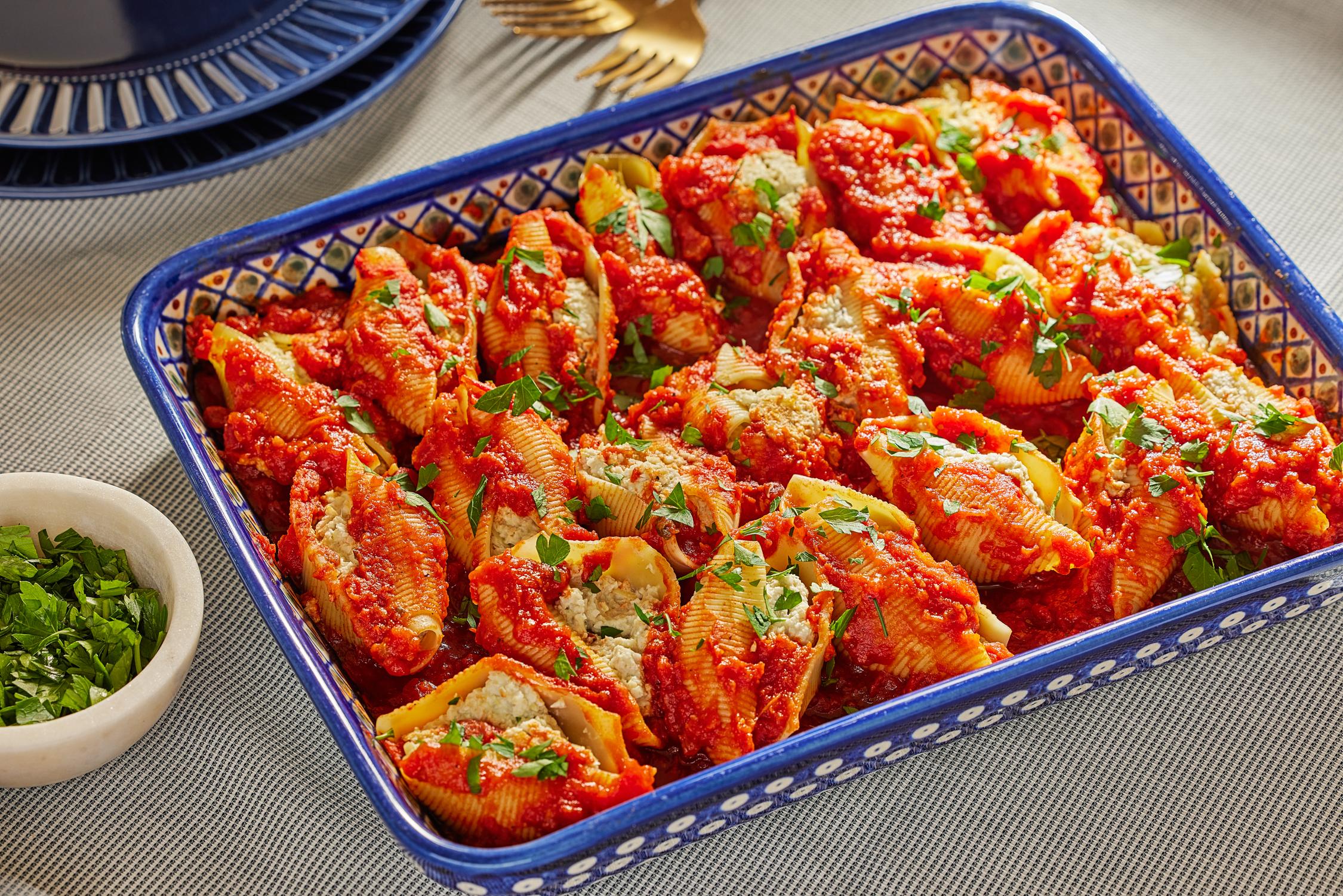 A shot of the creamy cashew cheese sauce being poured over the stuffed shells in the baking dish.