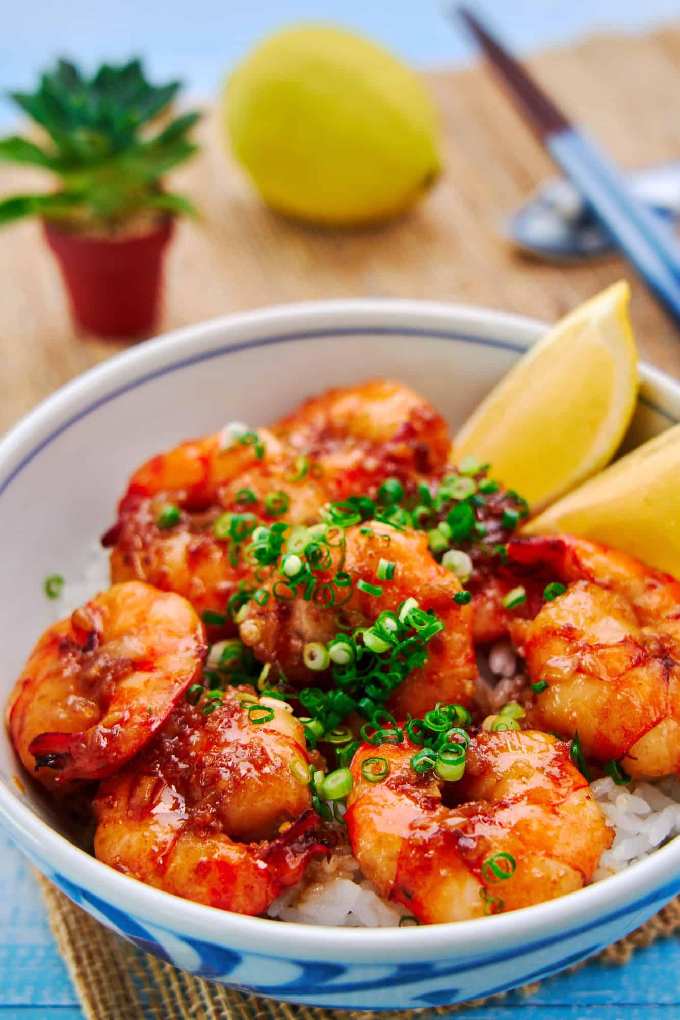 Close-up shot of vibrant pink prawns arranged on a bed of ice with a small bowl of chili garlic sauce on the side