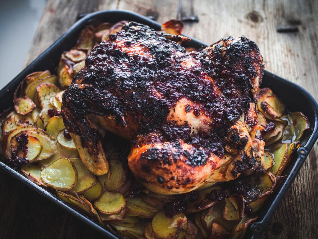 Close-up shot of the crispy skin of the roast chicken, glistening with melted herb butter and studded with lingonberries.