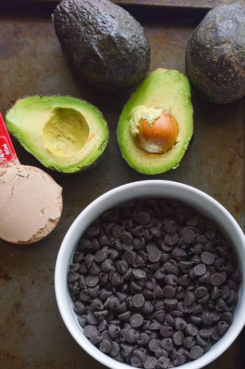A bowl of perfectly ripe avocados next to a bar of dark chocolate