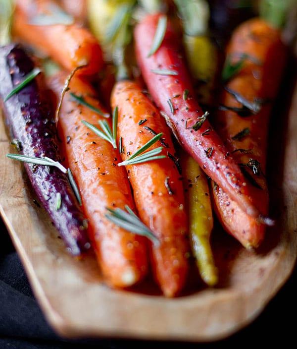 A person sprinkling rosemary over glazed carrots