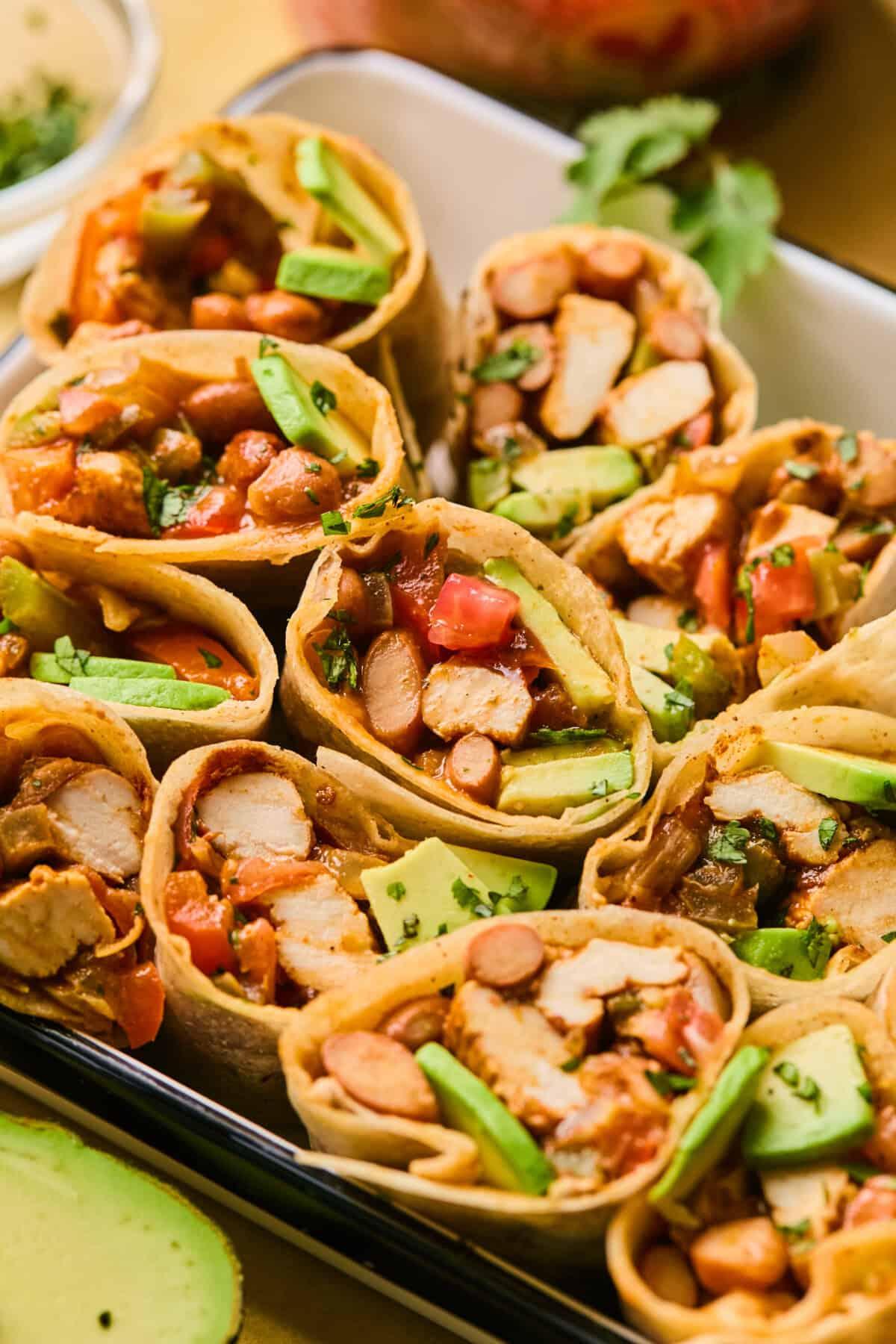 a variety of colorful toppings arranged around a plate of chicken taco wraps, showcasing customization options