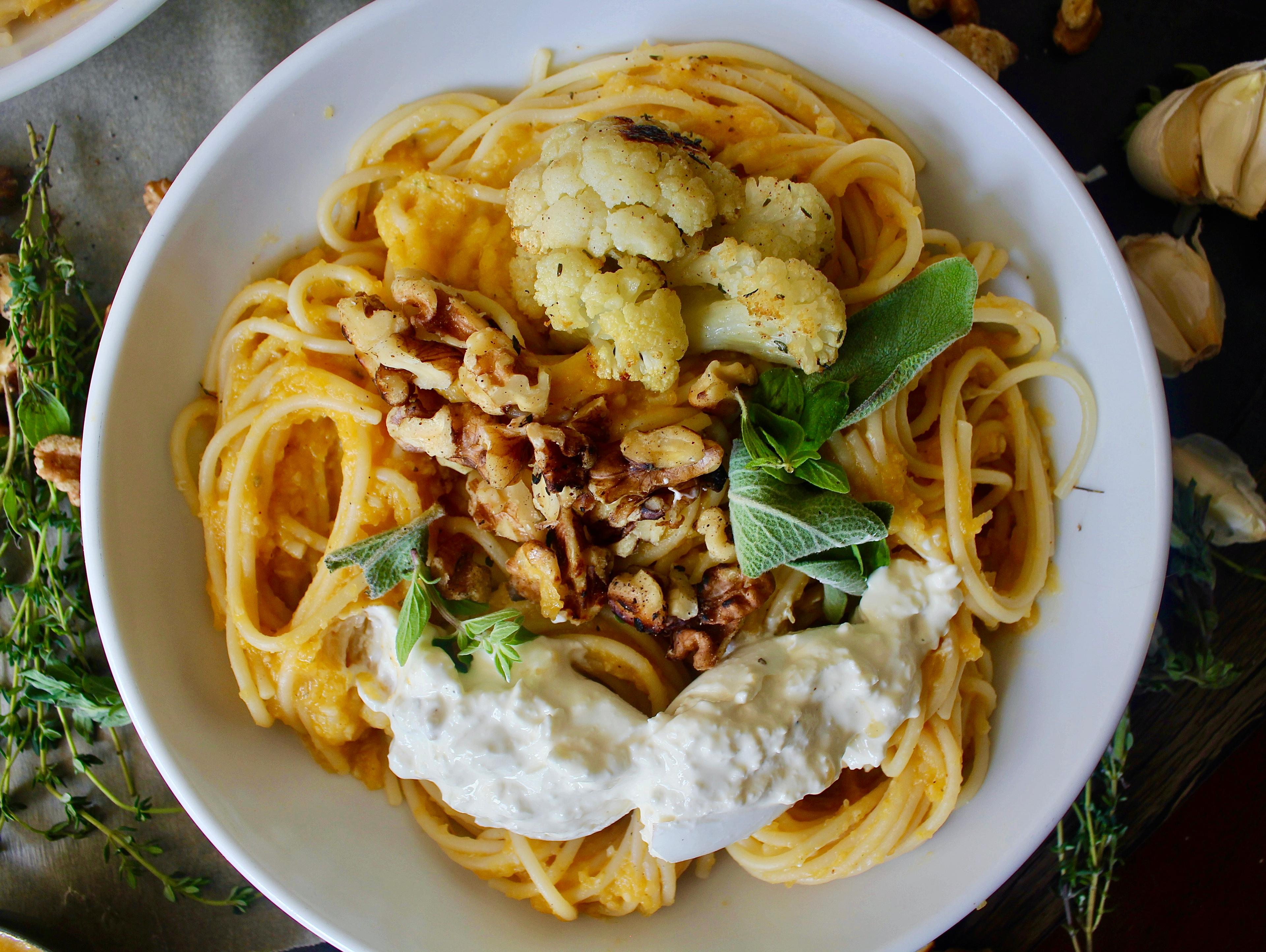 Close-up shot of a plate of butternut squash pasta with burrata and pesto