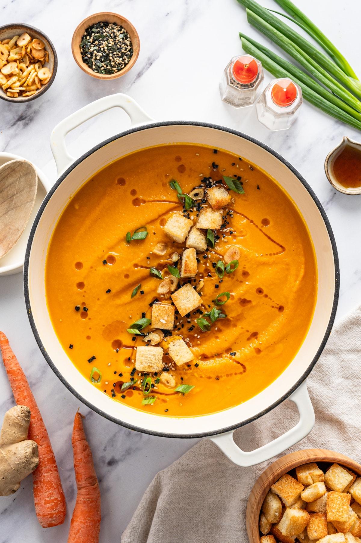 A vibrant bowl of creamy carrot and ginger soup garnished with toasted sesame seeds