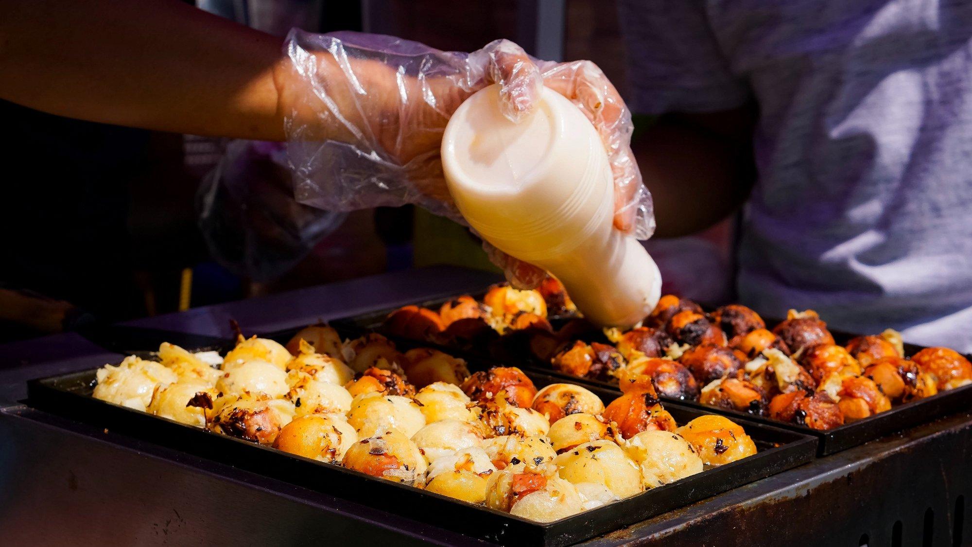 Friends gathered around a takoyaki pan, cooking together