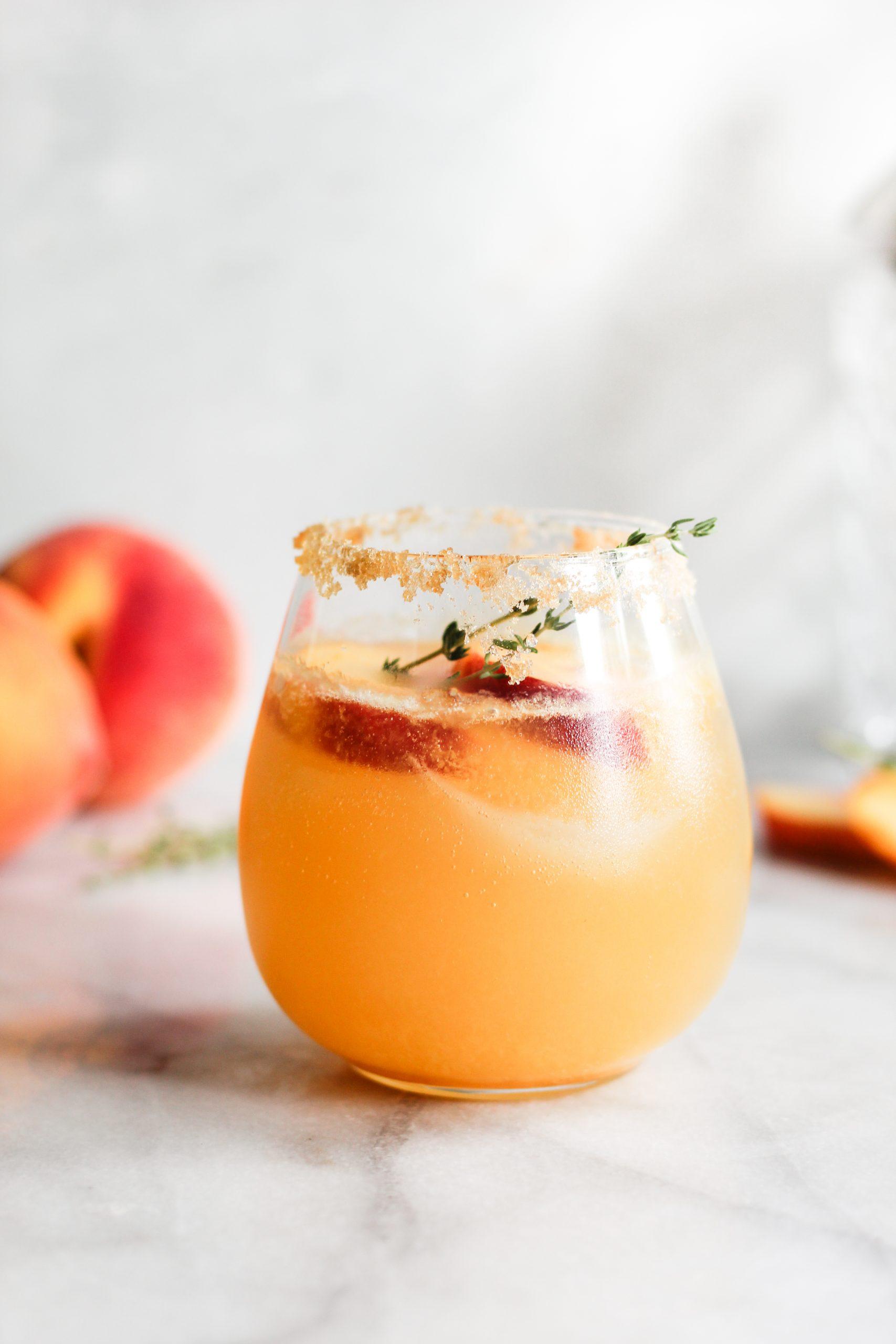 Close-up of a Peach Thyme Fizz cocktail in a highball glass, garnished with a sprig of thyme and a peach slice