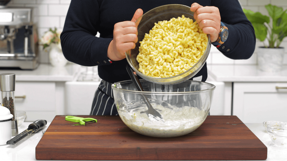 A person making macaroni salad, with a focus on the mixing process.