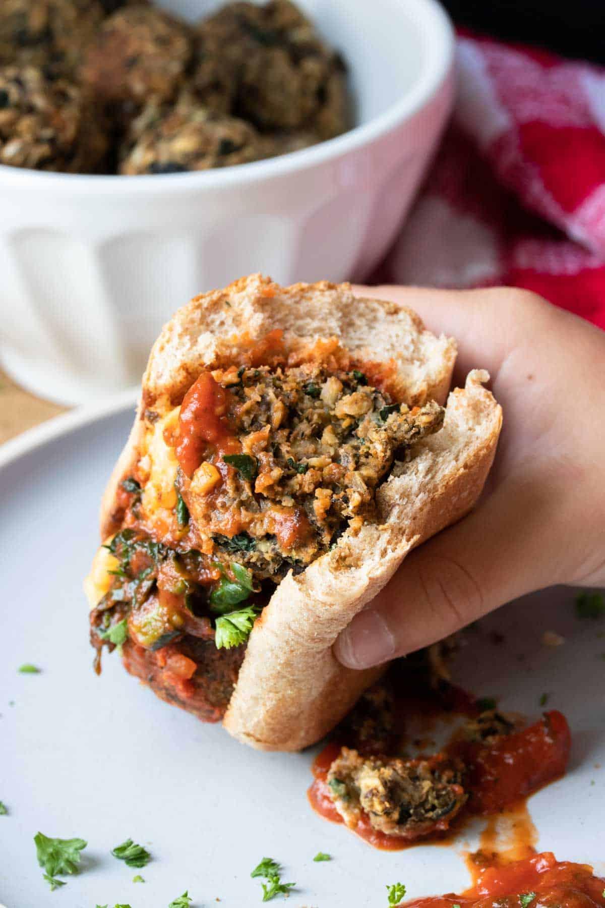 a person holding a half-eaten Philly cheesesteak plant-based meatball sub