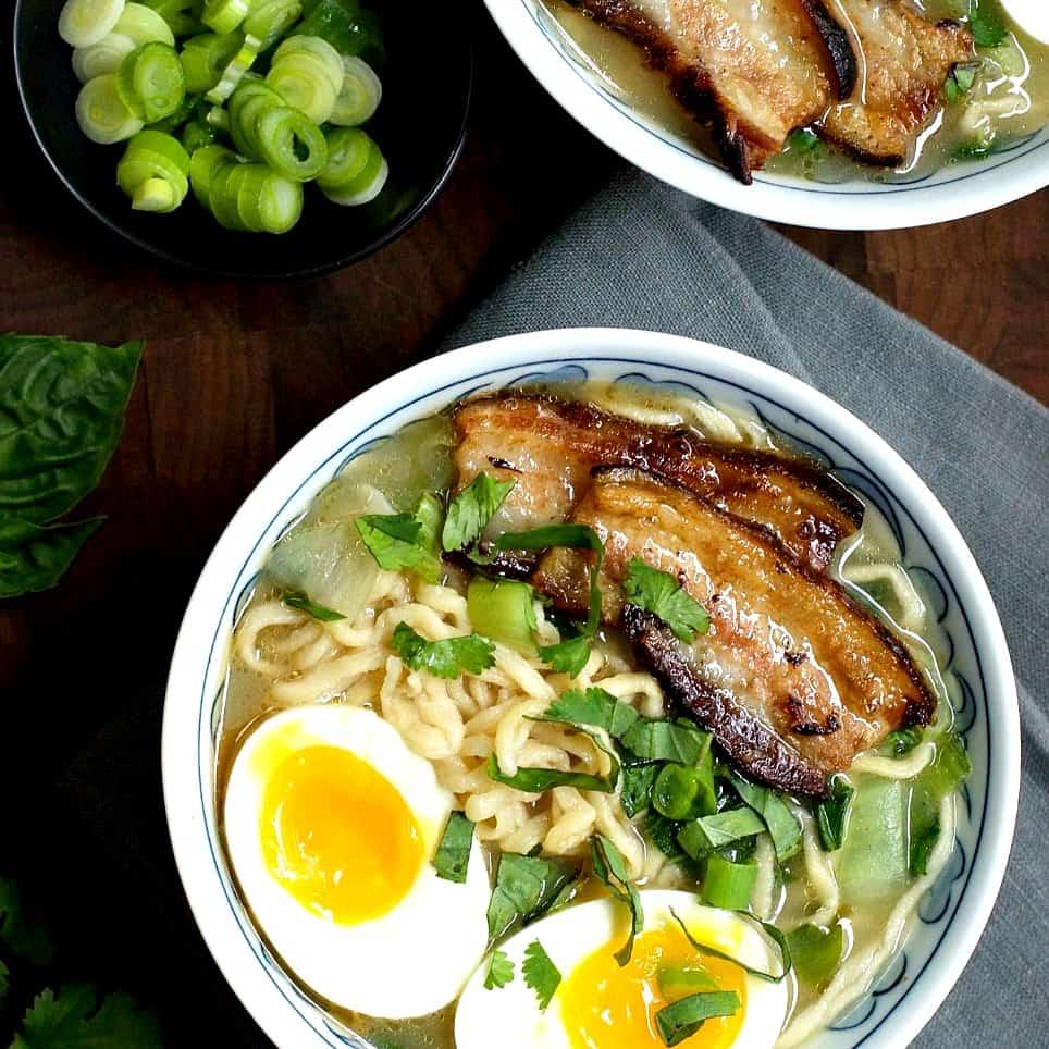 A steaming bowl of ramen with braised pork belly, pickled ginger, and fresh green onions