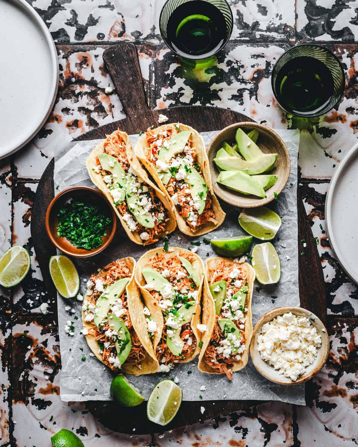 Tacos arranged on a rustic wooden table, garnished with lime slices and fresh cilantro
