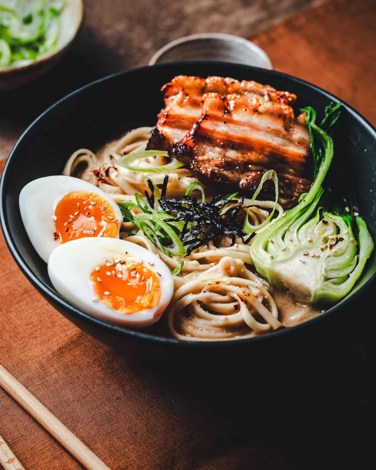 A steaming bowl of Miso Ramen topped with sesame seeds and garlic, garnished with scallions