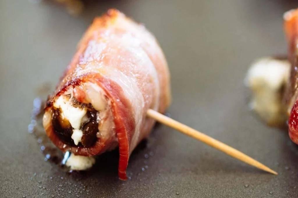 Close-up shot of a single bacon-wrapped date, showing the cheese filling