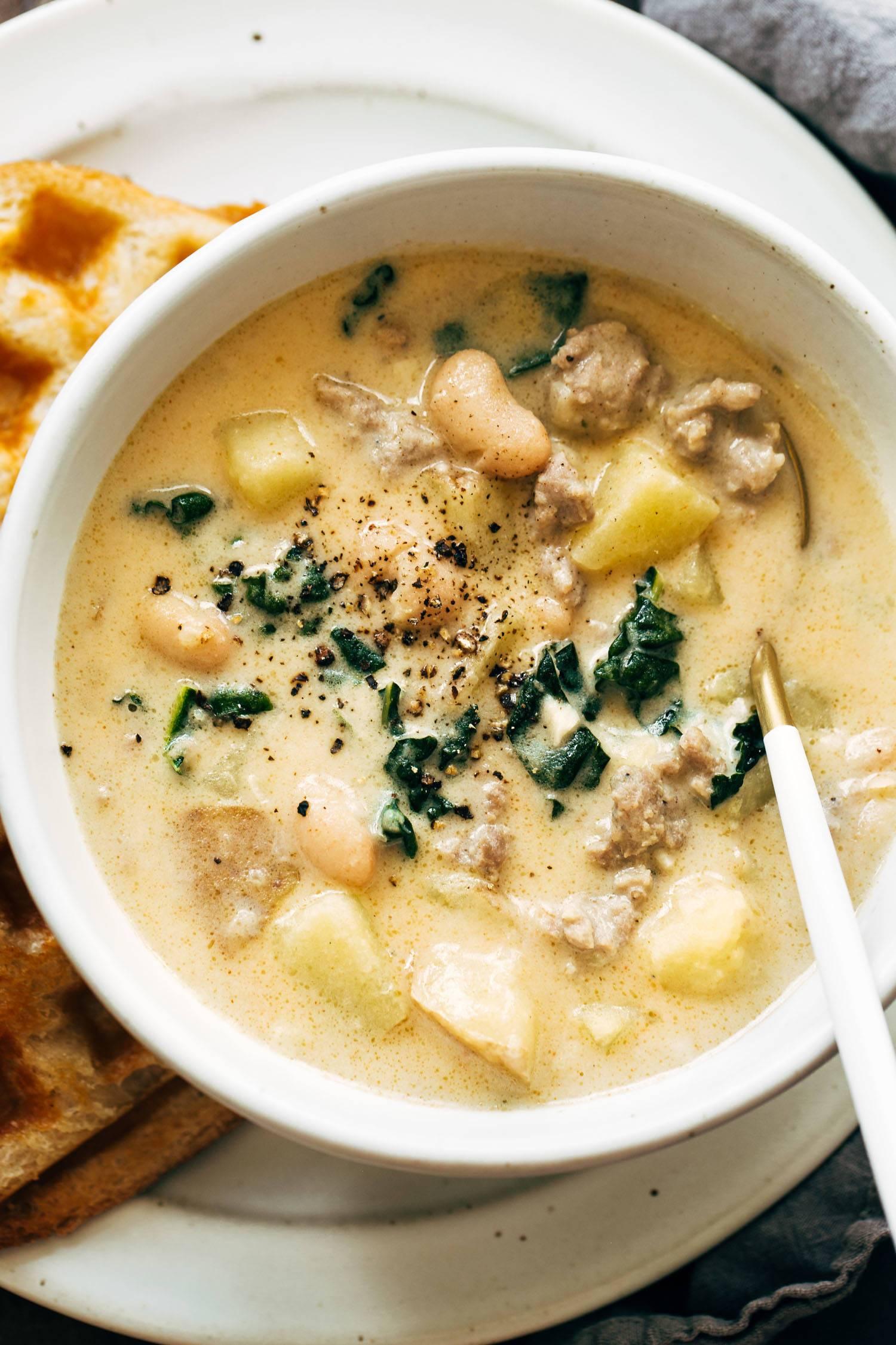 A person sitting at a table with a bowl of sausage and bean soup and a friend