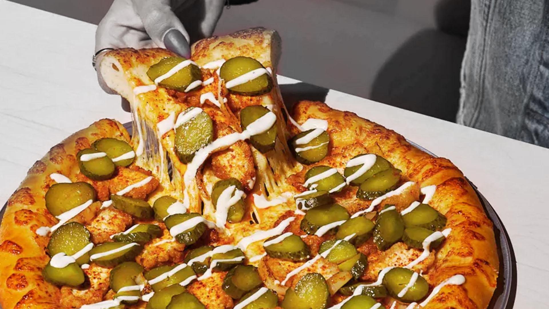 close-up shot of a slice of pickle pizza being lifted, showcasing the melted cheese and pickle slices