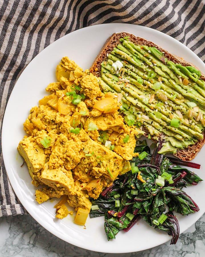 A close-up shot of a fluffy tofu scramble with mushrooms and thyme, garnished with fresh parsley.